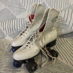 These are vintage Roller Derby brand roller skates featuring white high-top boots and urethane wheels.