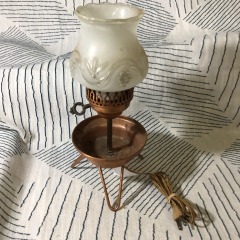 vintage candle lamp features a milk glass chimney with a floral design and a three-legged copper base