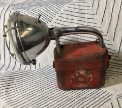 vintage Big Beam lantern features a prominent red metal battery housing with a hinged chrome-plated handle and a large adjustable spotlight attached to the top.